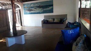 A room with a round table, a sofa with cushions, and a painting of a ship on the wall. - Kilindoni Sea View Bungalows (Mafia Island)