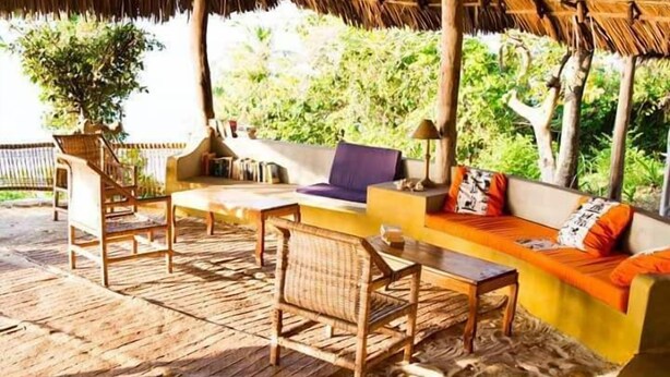 An outdoor seating area with wicker furniture, a sofa with orange cushions, and a thatched roof structure. - Kilindoni Sea View Bungalows (Mafia Island)