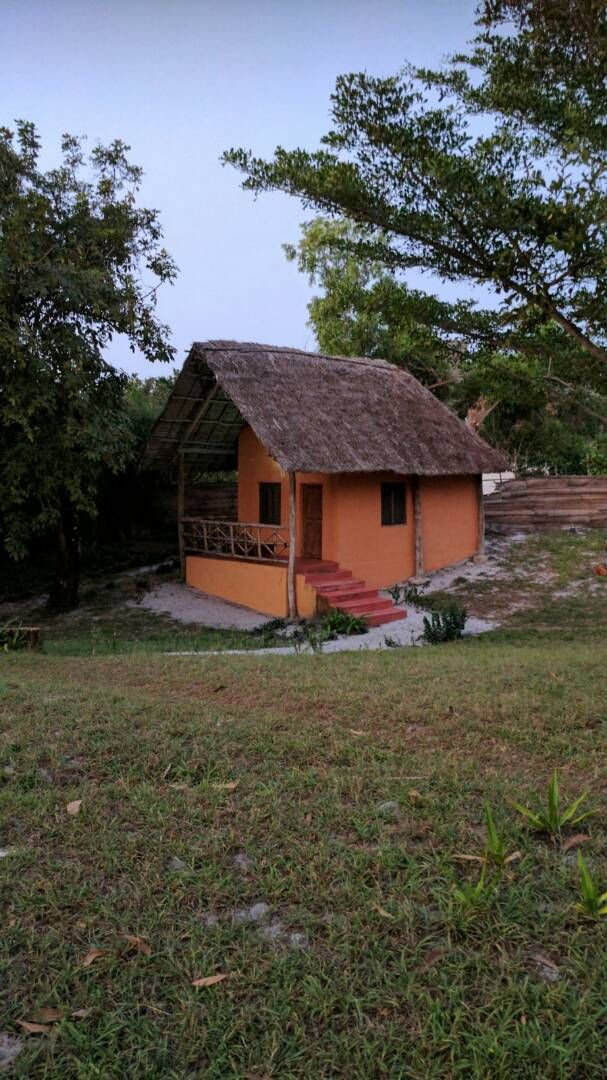 A small, single-story building with a thatched roof, a porch with a railing, and a staircase leading to the entrance.