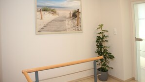Een hal met een houten bankje, een potplant en een wanddecoratie van een strandgezicht.