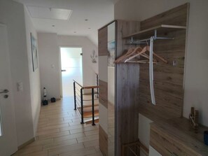 Een gang met houten vloer, een trap en een houten wand met kapstok.