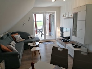 Ein modernes Wohnzimmer mit einer Couch, einem Fernseher und einem Essbereich mit Tisch und Stühlen.