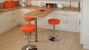Een moderne keuken met twee oranje barkrukken, een houten aanrecht en witte kasten.