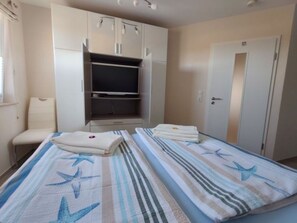 Ein Schlafzimmer mit zwei Betten, einem Kleiderschrank, einem Sessel und einem Fernseher.