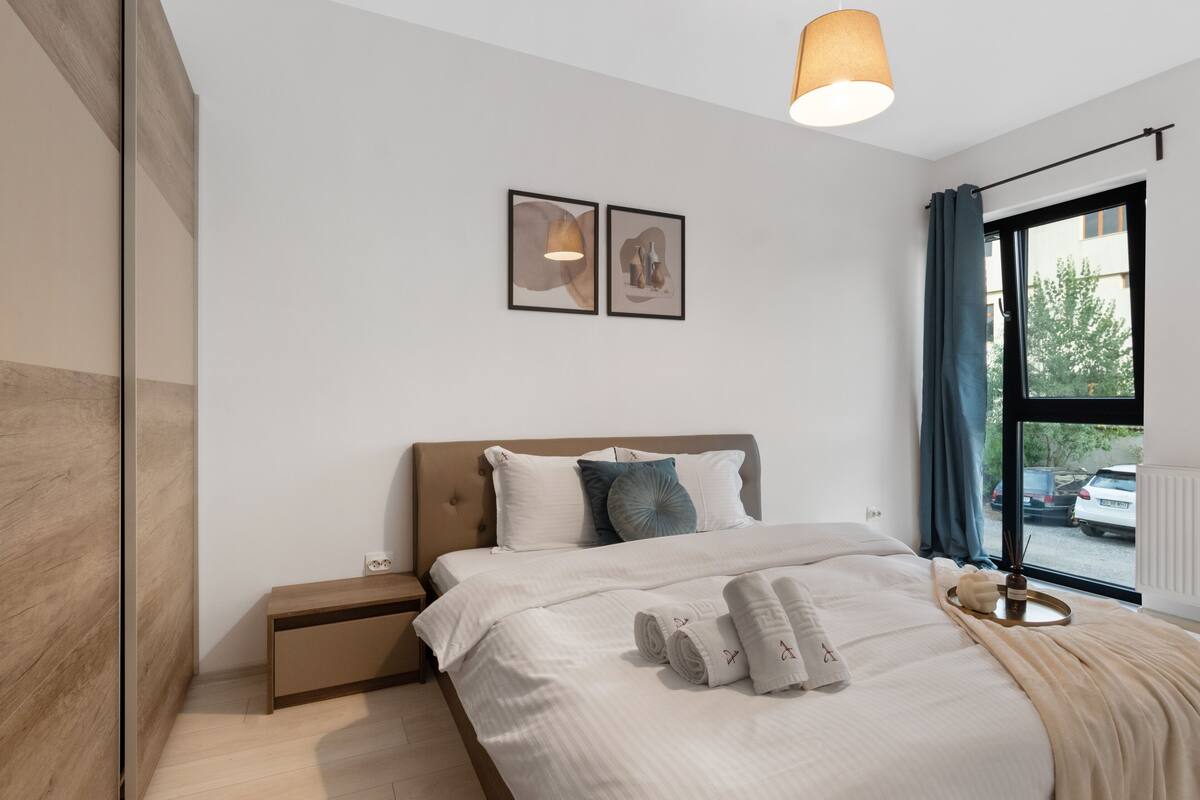 Un dormitorio moderno con cama, mesitas de noche, una ventana con cortinas y una obra de arte en la pared.