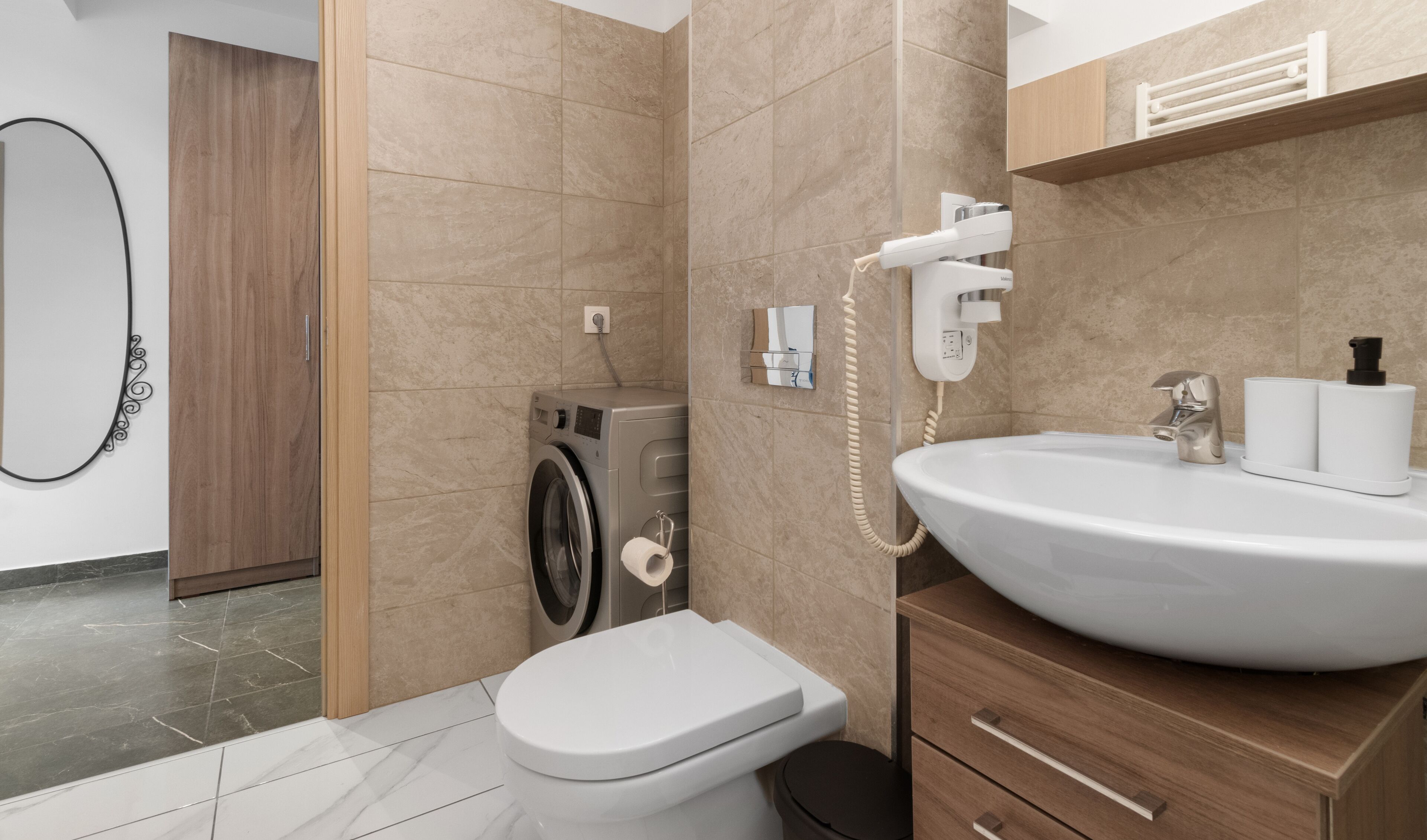 Een moderne badkamer met een ingebouwde wasmachine, toilet en een wastafel met spiegel.