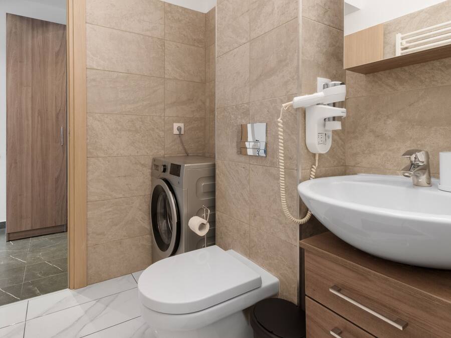 A modern bathroom with a built-in washing machine, a toilet, and a sink with a mirror above it.