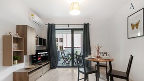 Una sala moderna con un televisor de pantalla plana, estanterías de madera, una zona de comedor con mesa y sillas, y un ventanal corredizo que da a un patio exterior.