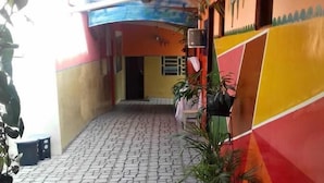 Um corredor estreito e pavimentado, com plantas em vasos de ambos os lados, que leva a uma porta no final.