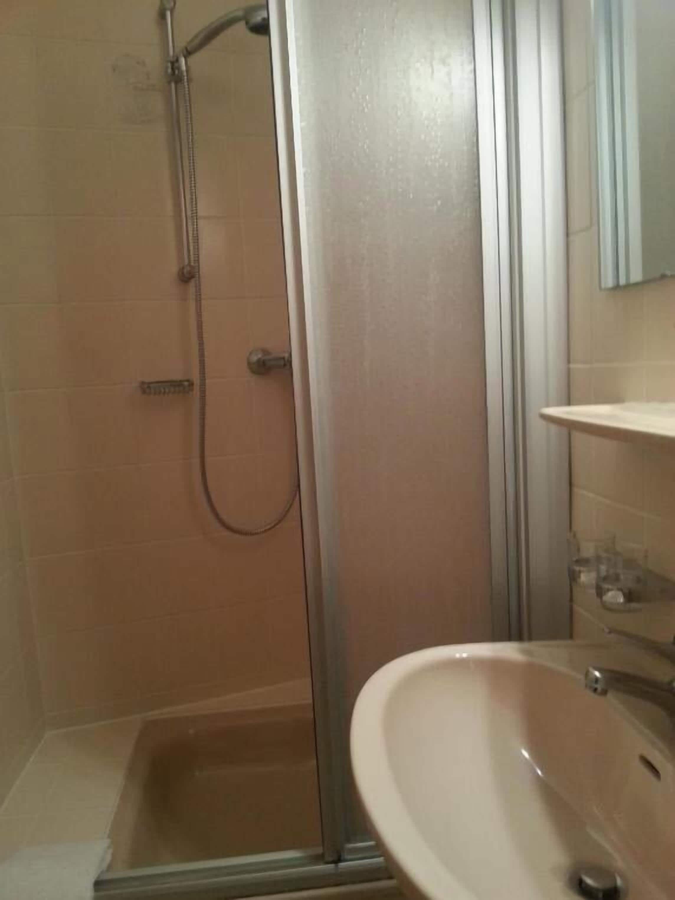 Un baño con ducha de mampara de vidrio, lavabo y espejo.