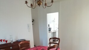 Ein Essbereich mit einem Tisch, bedeckt mit einer blumigen Tischdecke, zwei Holzsesseln und einem Sofa.