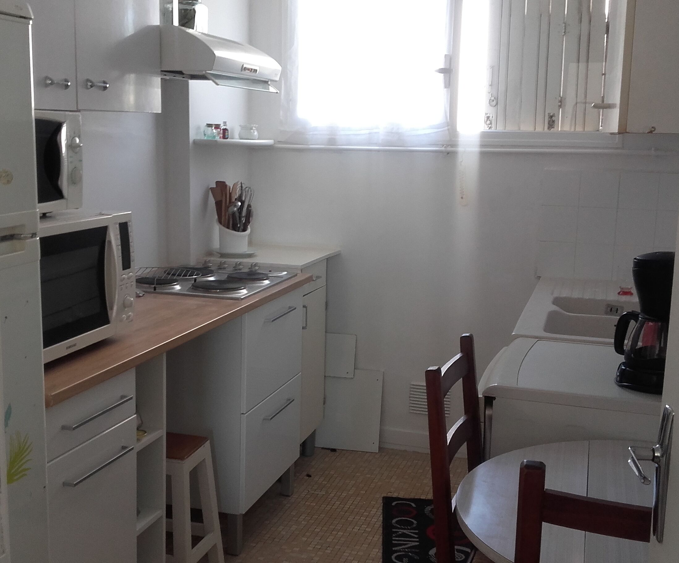 A compact kitchen with a microwave, stove, and sink. There is a wooden countertop and a chair at a small table.