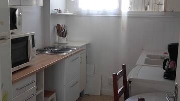 A compact kitchen with a microwave, stove, and sink. There is a wooden countertop and a chair at a small table.