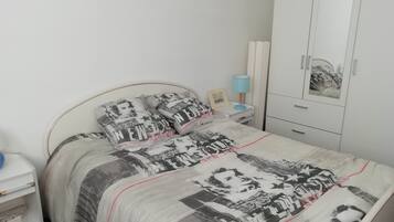 A bedroom with a bed featuring a patterned bedspread, a bedside table with a lamp, and a wardrobe.