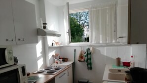 Eine Küche mit weißen Schränken, einer Mikrowelle, einem Herd und einem Fenster mit Vorhängen.