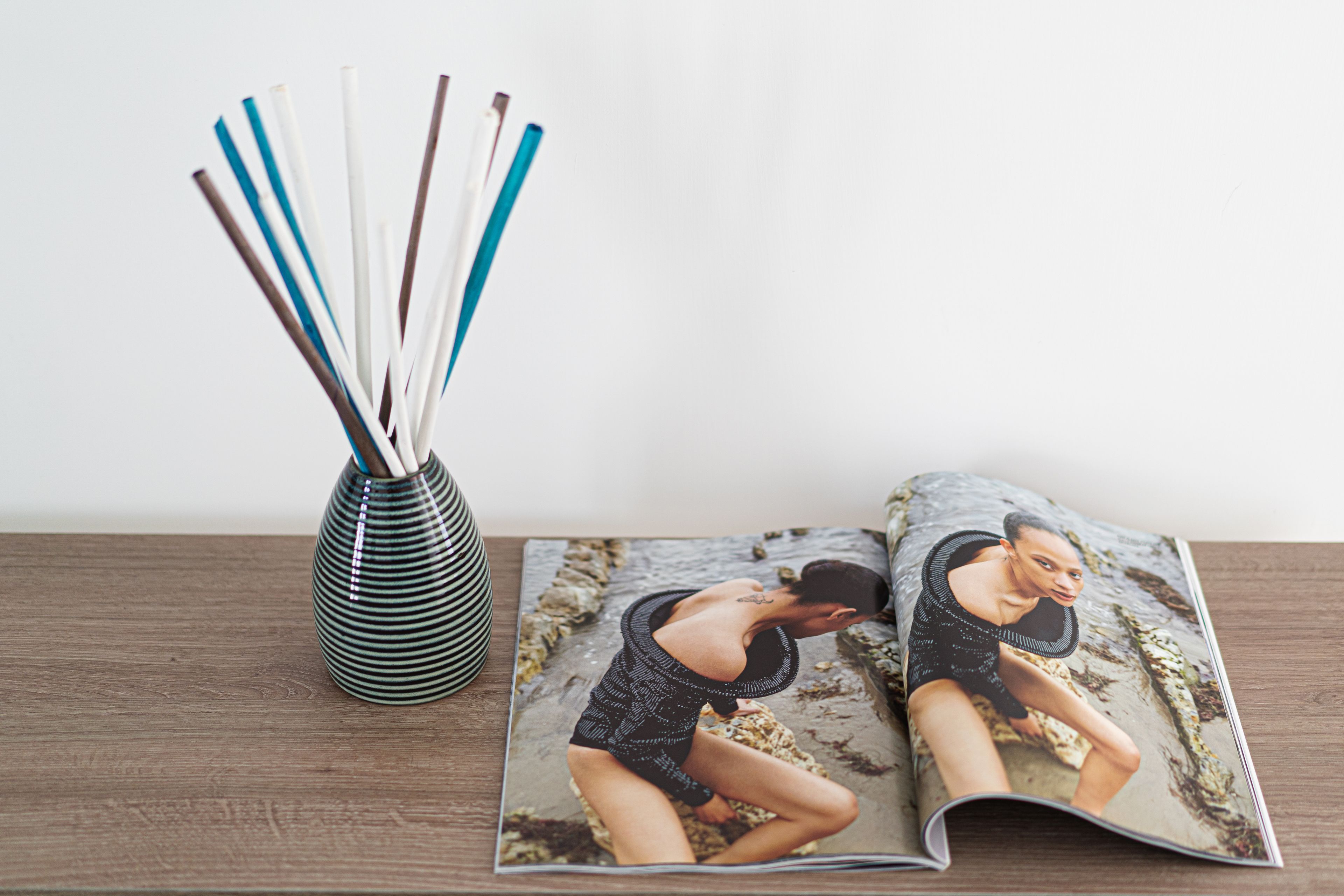 A magazine with a beach scene on the cover, a striped vase, and wooden table.