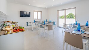 A modern dining area with multiple tables and chairs, a kitchen counter with food and drinks, and a TV mounted on the wall. - Do'Petro (Vico Equense)