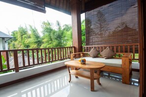 A wooden balcony with a sofa and a table, surrounded by a wooden railing. - Flamboyant Villa Ubud (Ubud)