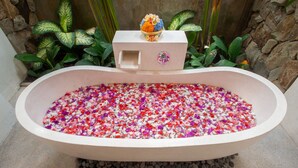 Una bañera llena de pétalos de flores multicolores, rodeada de plantas y un muro de piedra.