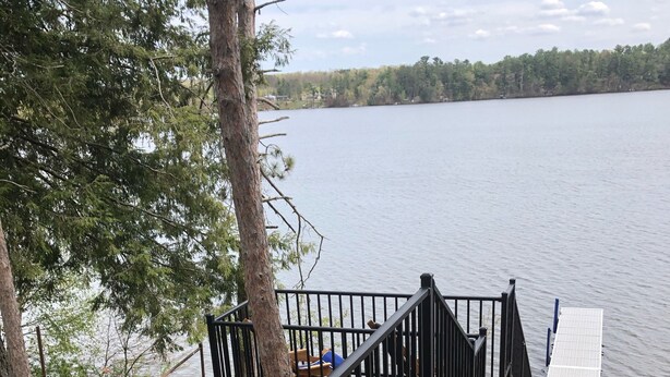 Eine Holzterrasse mit schwarzen Geländern, die zu einem See führt.