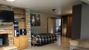 Ein Wohnzimmer mit Kamin aus Stein, einem Bett mit kariertem Überwurf, einem Fernseher und einem Wandbild von Hunden.