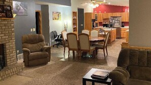 Ein Wohnzimmer mit Kamin, eine Essecke mit Tisch und Stühlen sowie eine Küche mit Holdekor und Kühlschrank.