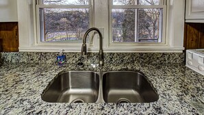 Una cocina con encimera de granito, pileta doble de acero inoxidable y una ventana sobre la pileta.