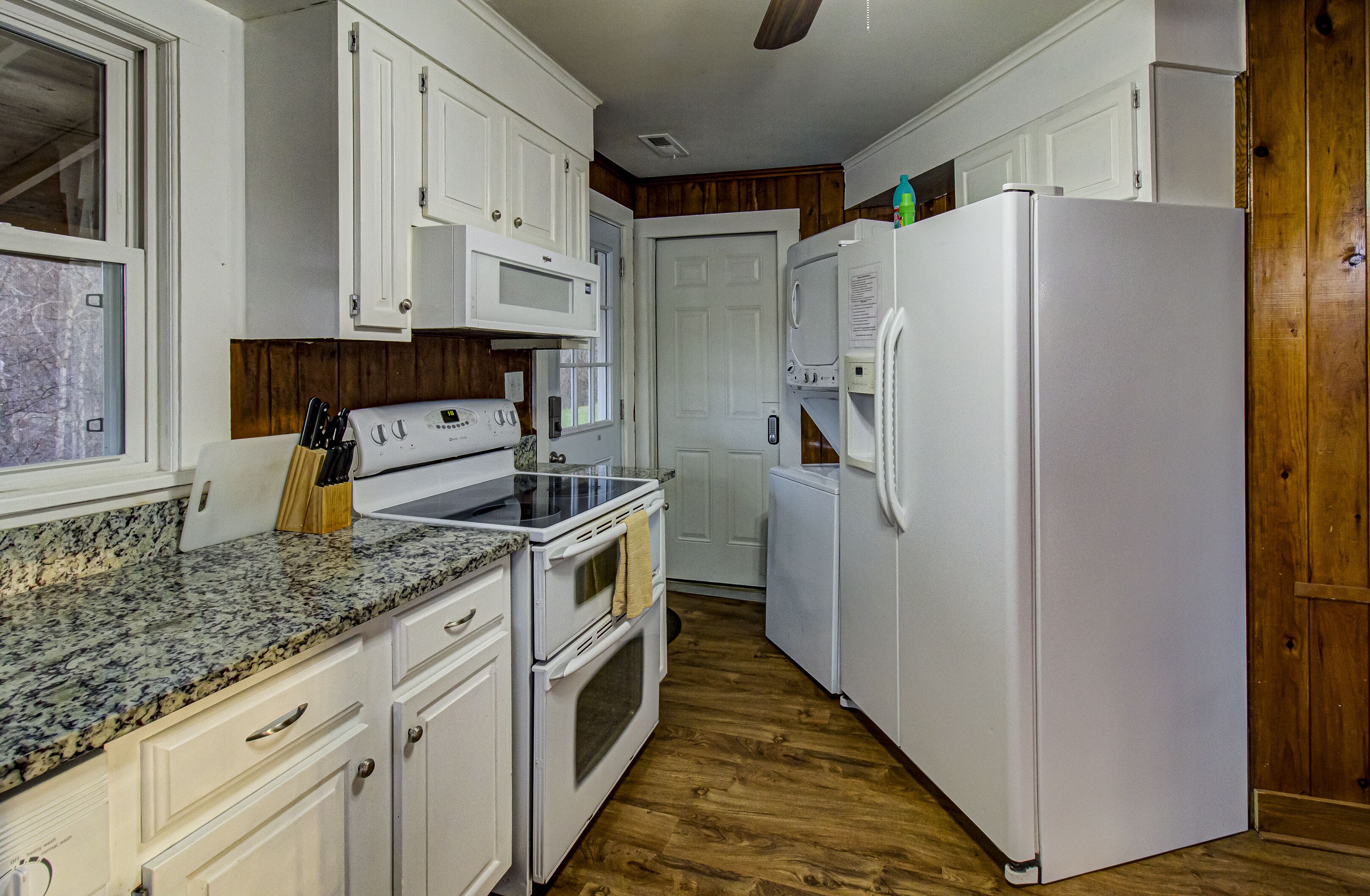 A kitchen with white cabinets, a granite countertop, a stove, a microwave, and a refrigerator.