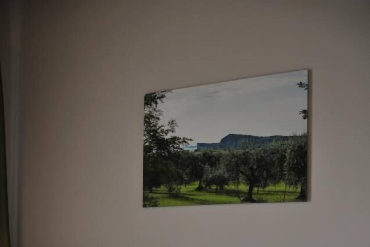 Un lit bien fait, avec des serviettes blanches pliées et un ruban vert, un tableau représentant un paysage accroché au mur, et une lampe de chevet.
