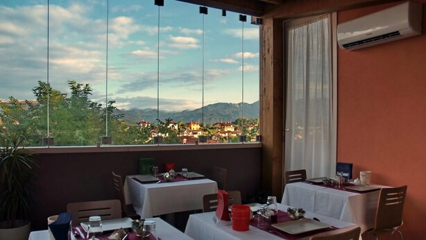 Ein Restaurant mit gedeckten Tischen, Blick auf eine Stadt und Berge sowie eine Klimaanlage an der Wand.