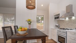 A modern kitchen with a wooden dining table, white cabinets, and a built-in oven. - Enjoy this piece of paradise and immerse yourself in luxury and style. (Byron Bay)