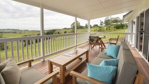 A covered outdoor deck with a wooden table, chairs, and a sofa with cushions. - Enjoy this piece of paradise and immerse yourself in luxury and style. (Byron Bay)