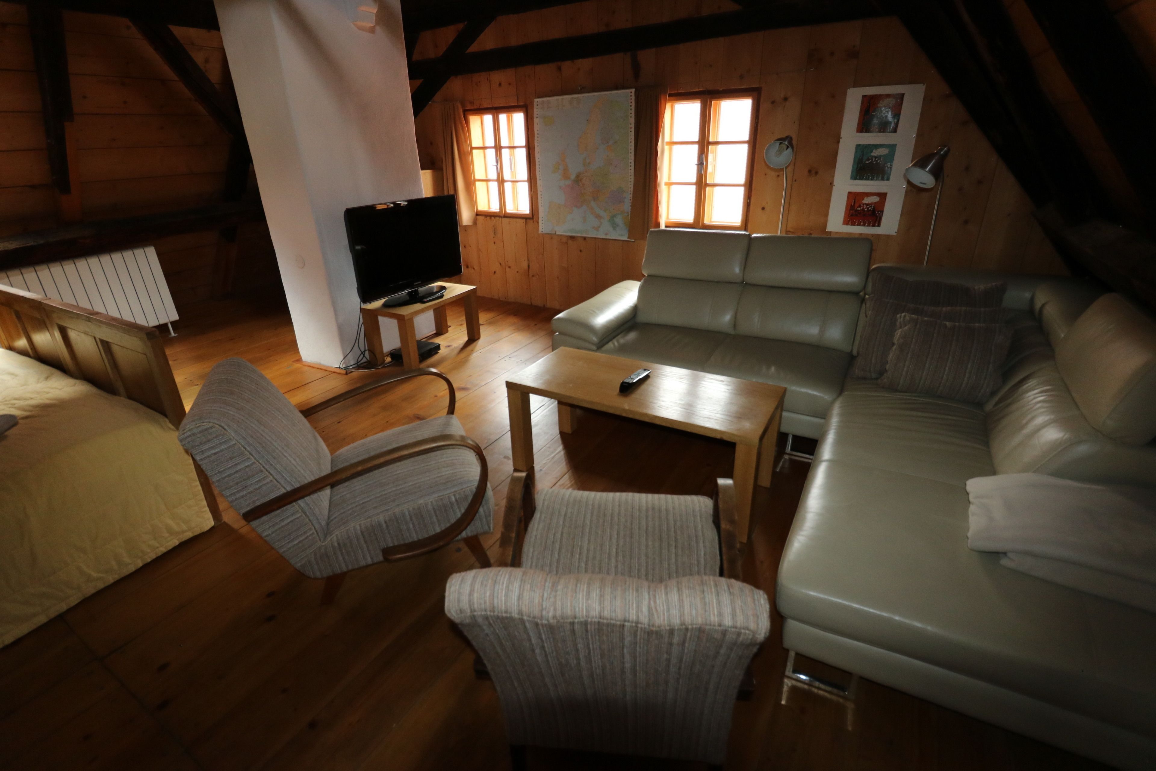 A cozy attic room with a wooden ceiling, a sofa, a chair, a small table, and a television.