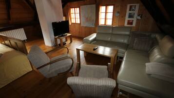 A cozy attic room with a wooden ceiling, a sofa, a chair, a small table, and a television.