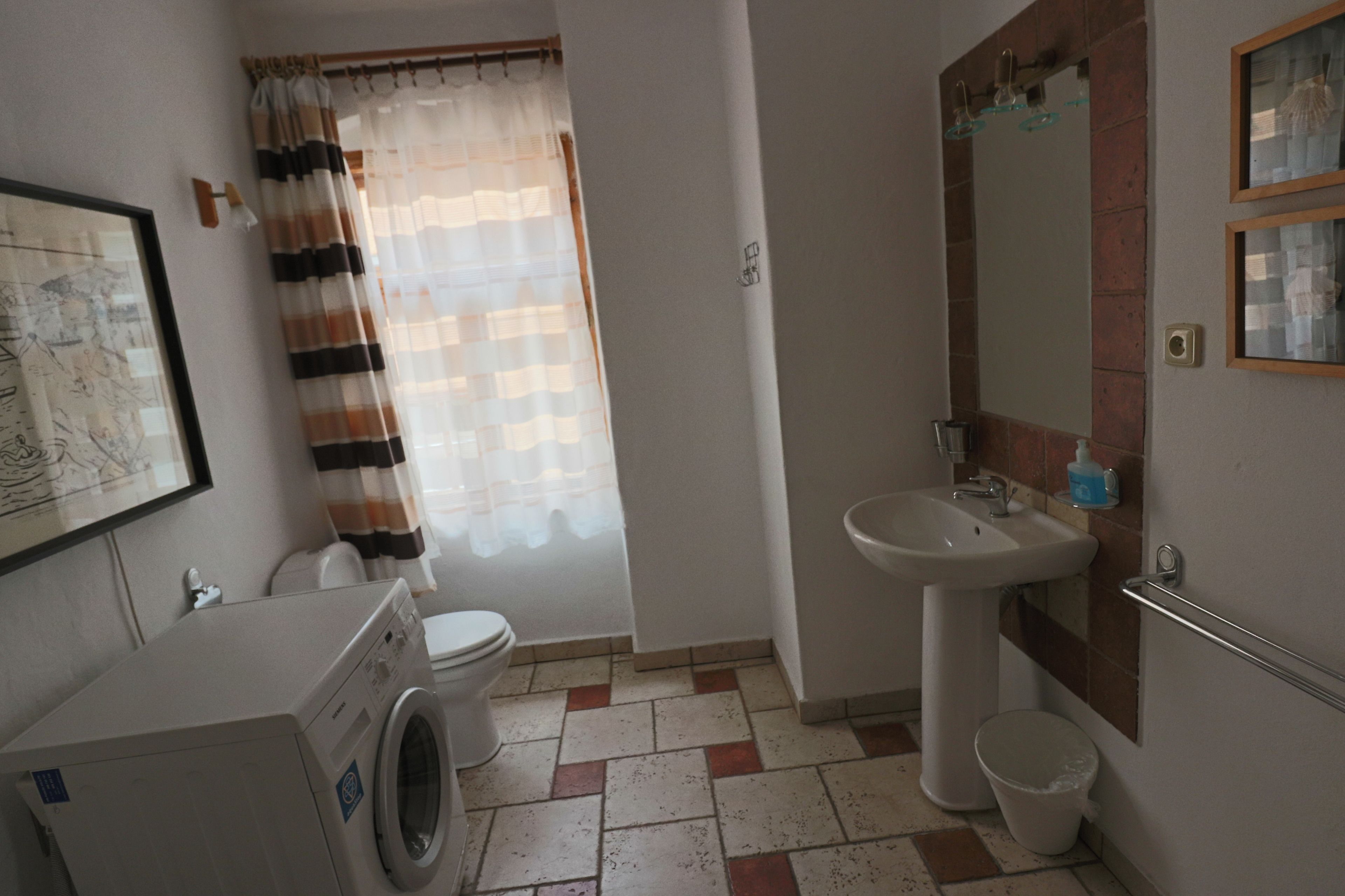 A small bathroom with a washing machine, toilet, sink, and a shower curtain.