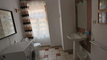 A small bathroom with a washing machine, toilet, sink, and a shower curtain.