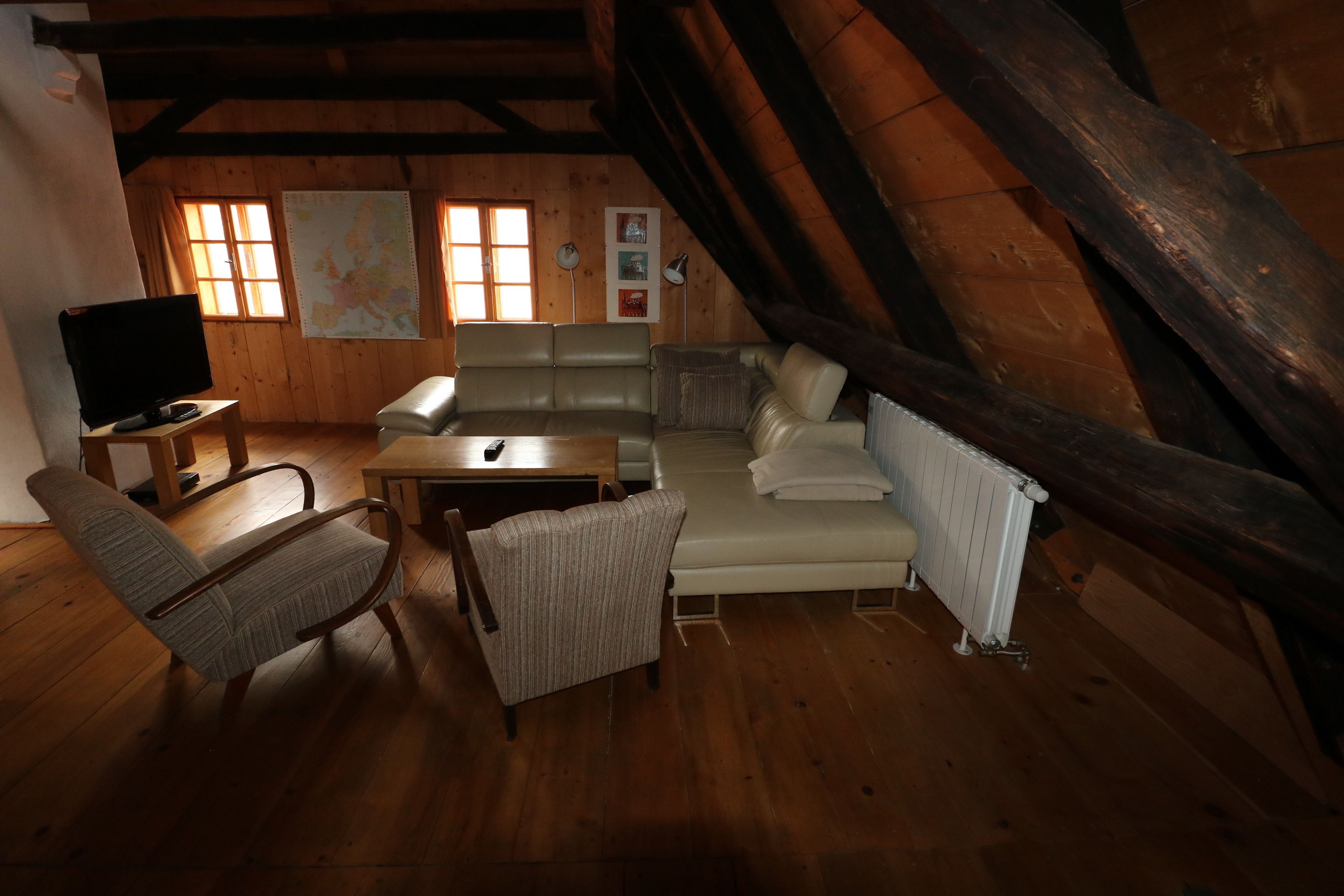 Ein gemütliches Schlafzimmer im Dachgeschoss mit Holzbalkendecke, einem Sofa, einem Sessel, einem kleinen Tisch und einem Fernseher.