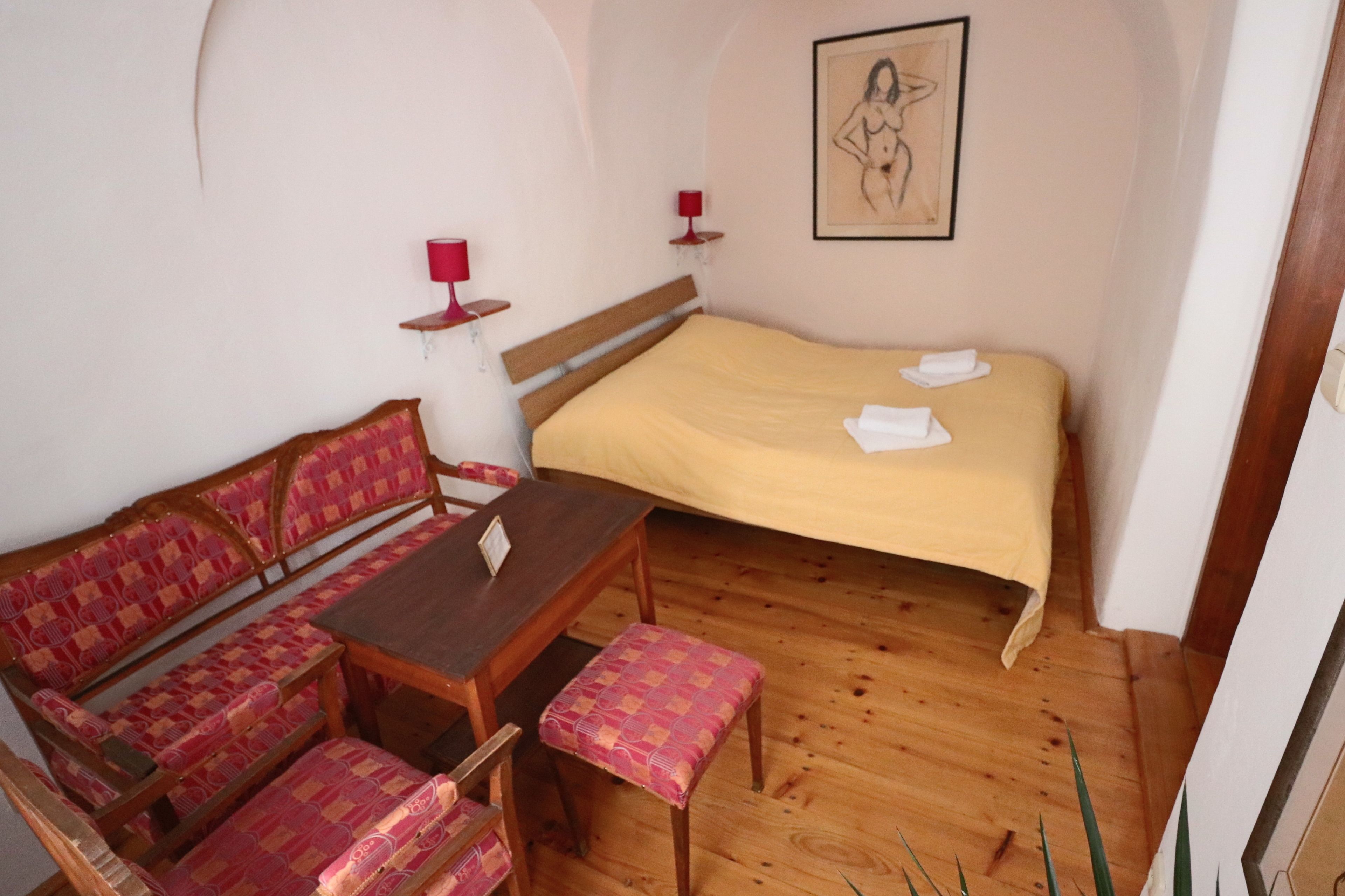 A room with a bed, a wooden bench, a table, and a wall-mounted picture.