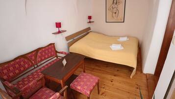 A room with a bed, a wooden bench, a table, and a wall-mounted picture.