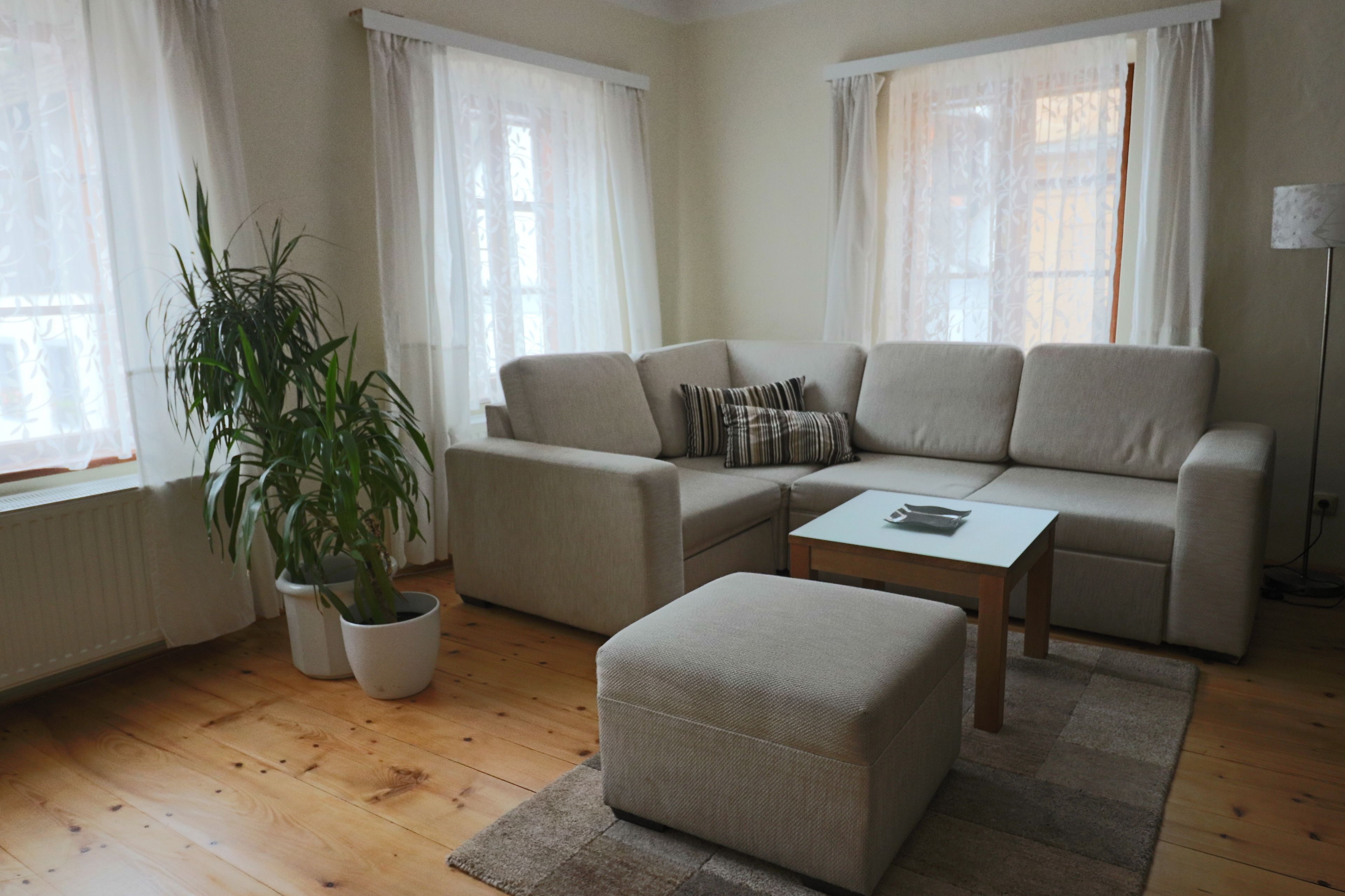Een woonkamer met een beige bank, een bijpassend voetenbankje, een houten salontafel en een plant in een pot.