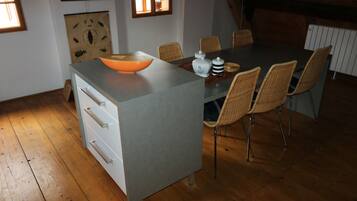 A dining area with a grey table, wicker chairs, and a white cabinet with drawers.