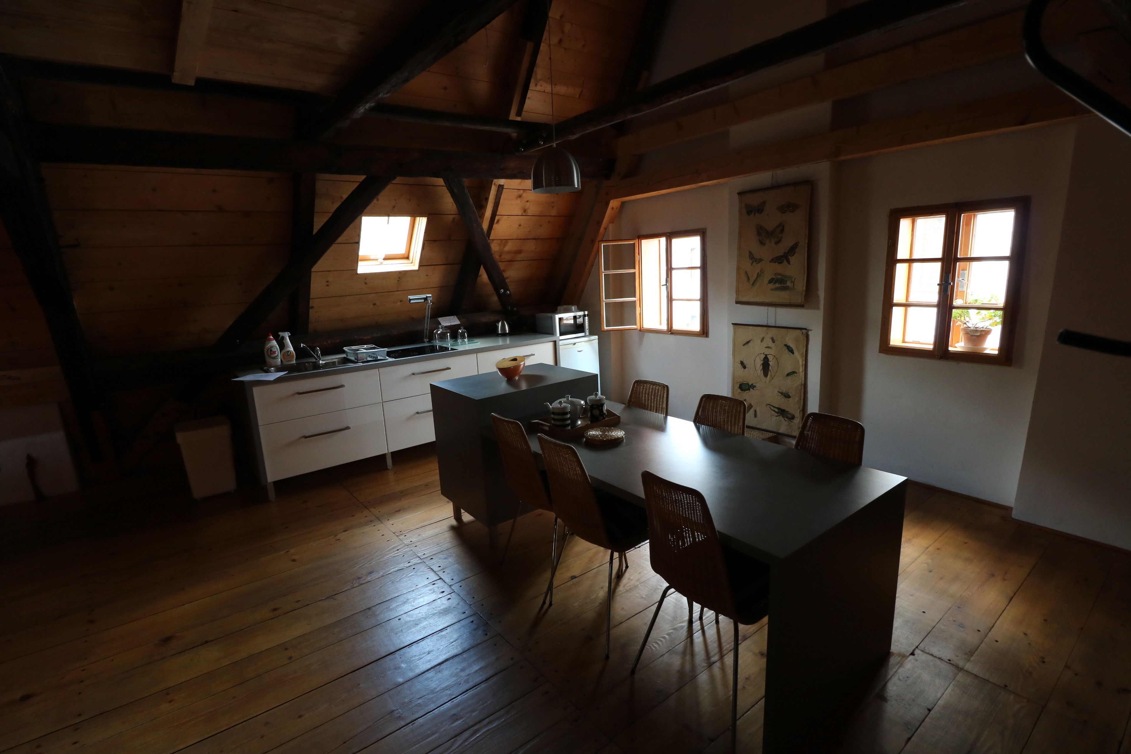 Une cuisine rustique avec des poutres en bois, une table à manger entourée de chaises et une fenêtre donnant sur l’extérieur.