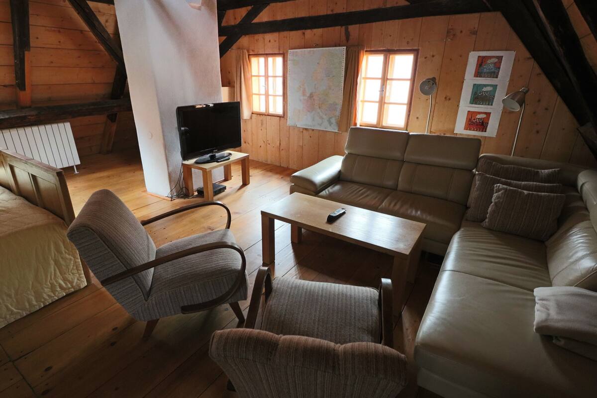 Ein gemütliches Dachzimmer mit Holzboden, einer Couch, einem Sessel, einem kleinen Tisch, einem Fernseher und einer Karte an der Wand.