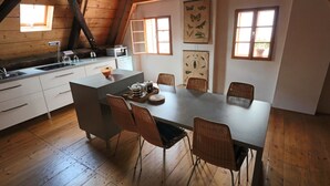 A modern kitchen with wooden beams, a dining area with wicker chairs, and a view of the outdoors through windows. - Apartment Soukenická 44 (Cesky Krumlov)