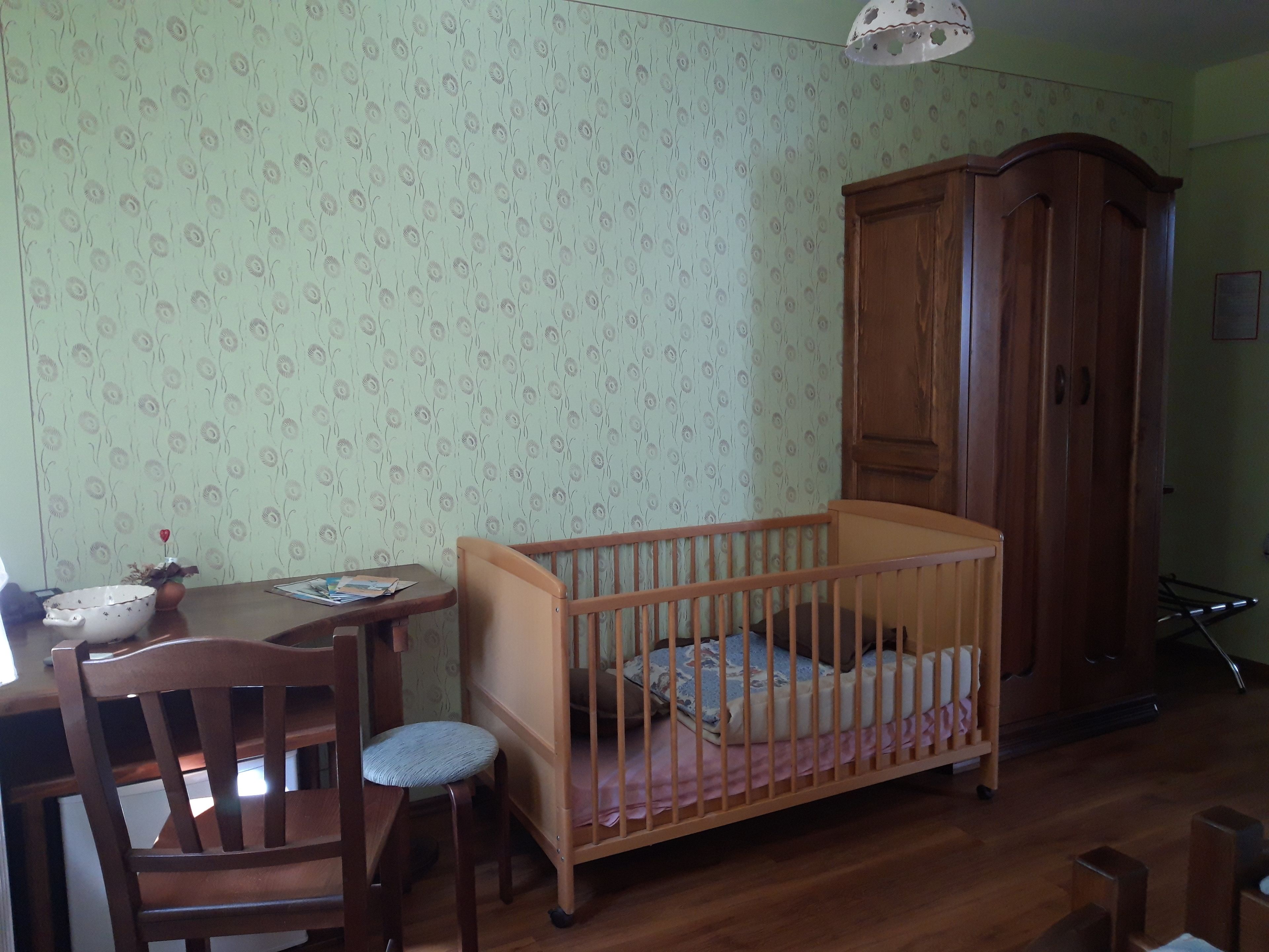 Ein Zimmer mit einem hölzernen Kinderbett, einem Holzschrank, einem Esstisch mit Stühlen und wanddekoriertem Zierpapier.