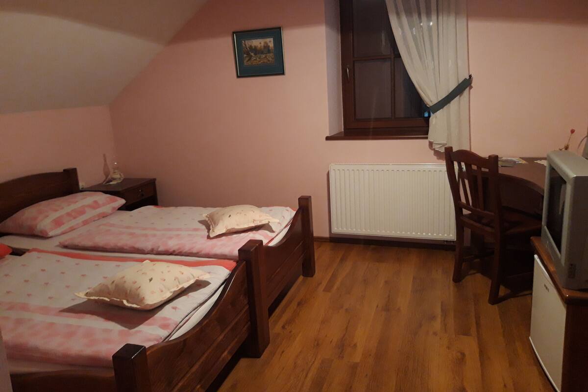 Ein Schlafzimmer mit zwei Einzelbetten, einem Holzstuhl, einem kleinen Tisch, einem Heizkörper und einem Fernseher.