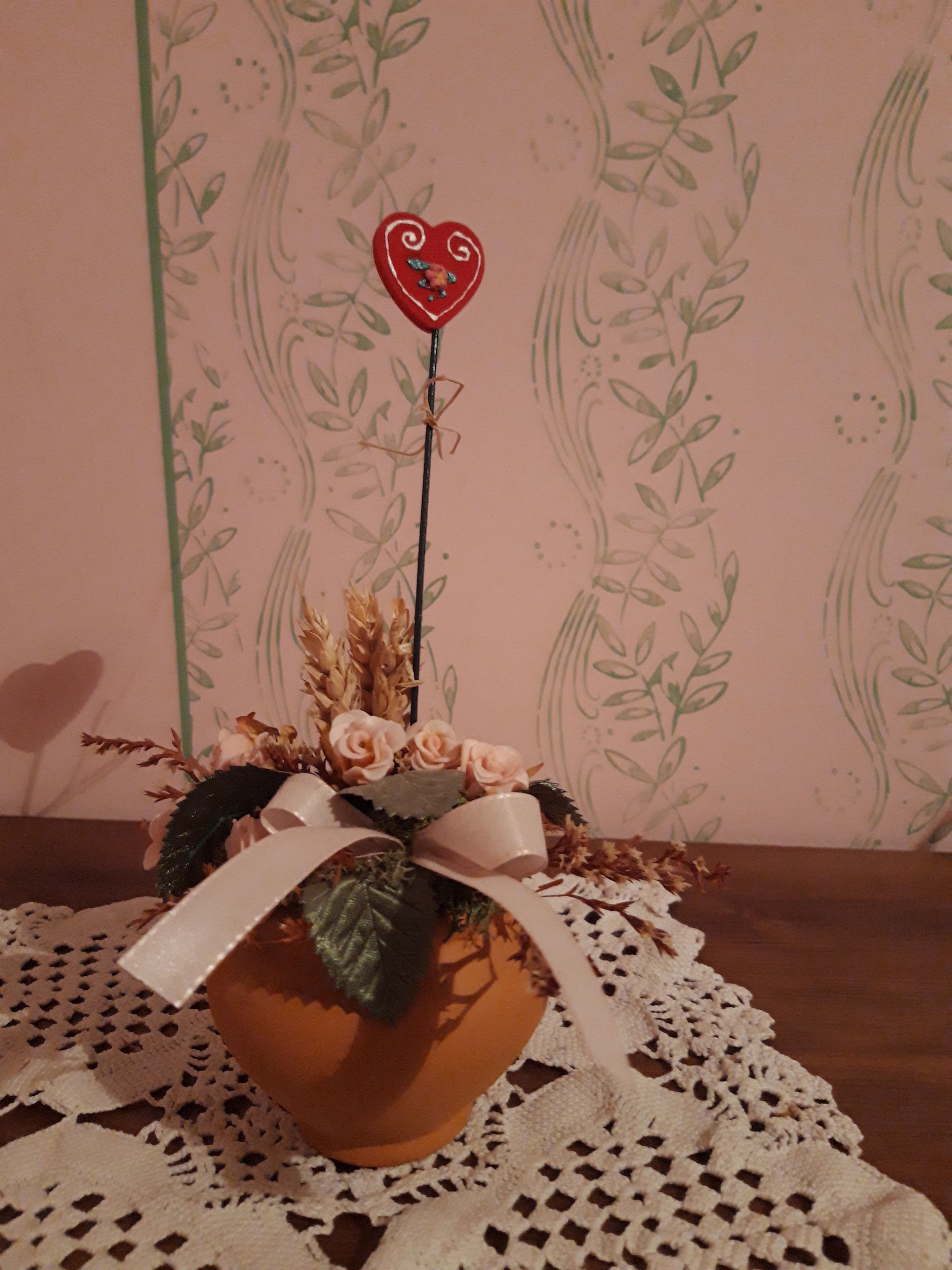 A potted plant with a heart-shaped decoration on a doily.