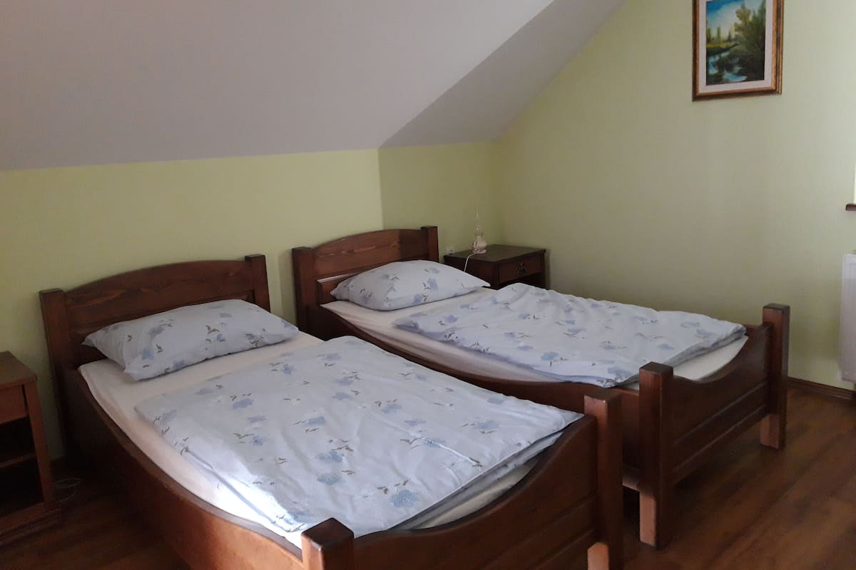 Ein schlichter, kleiner Raum mit zwei Holzbett, einem Nachttisch mit Lampe und einem gerahmten Bild an der Wand.