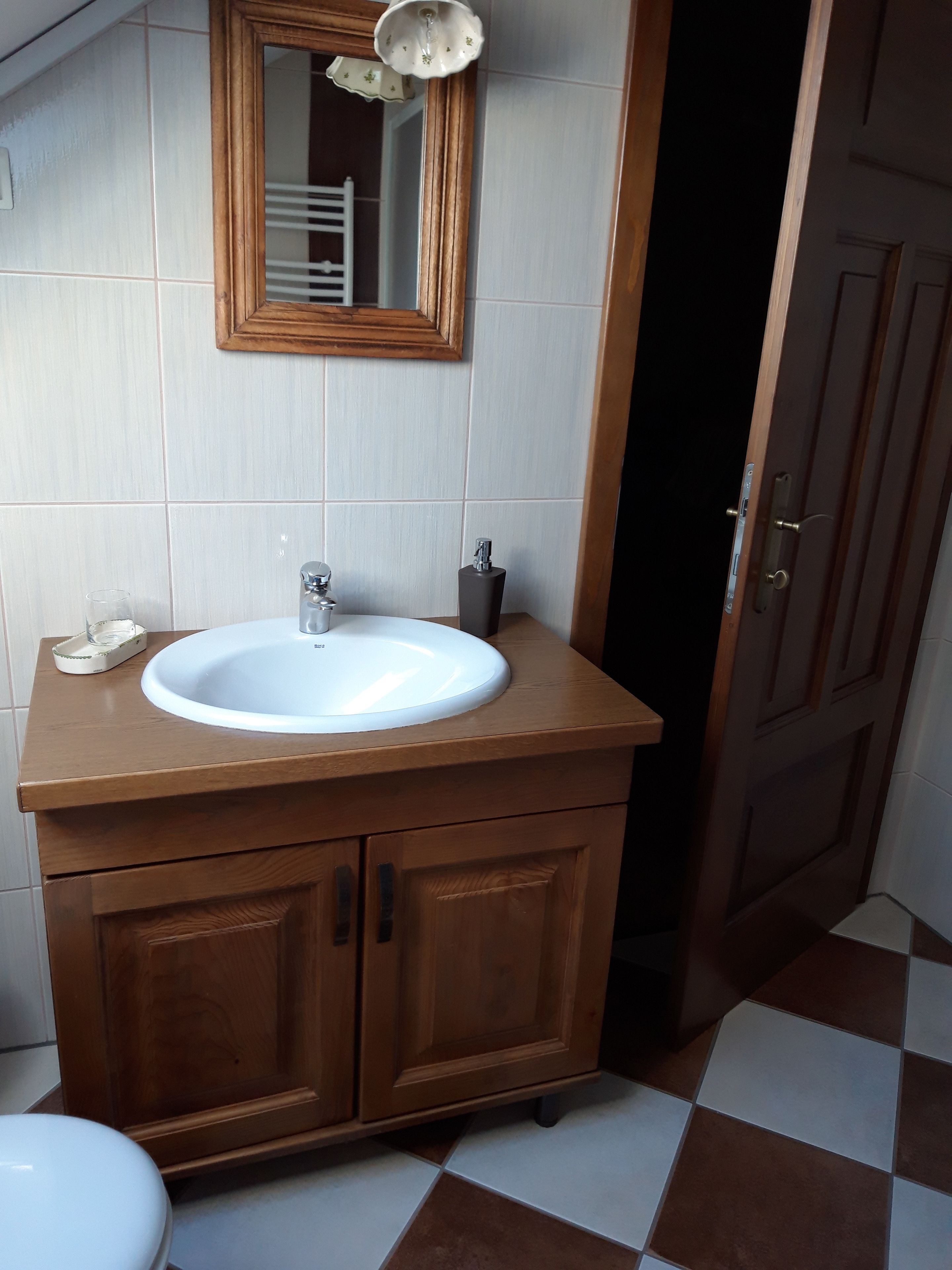 Een badkamer met een houten wastafelmeubel, een witte wasbak en een spiegel erboven.