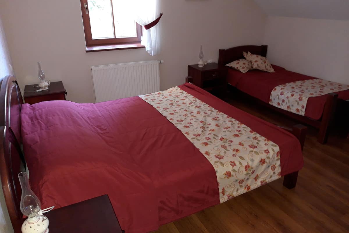 Ein Schlafzimmer mit zwei Einzelbetten, einem Heizkörper, einem Fenster mit Vorhängen, einem Nachttisch mit Lampe und einem Holzboden.